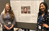Two female research students standing in front of a research poster board