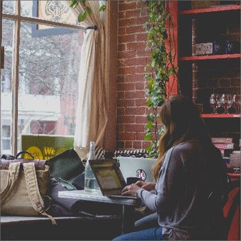 A woman working on something on her laptop in front of a window.