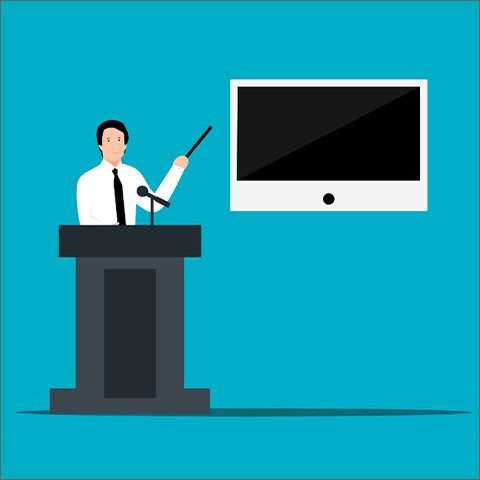 A speaker on a podium pointing at a screen.