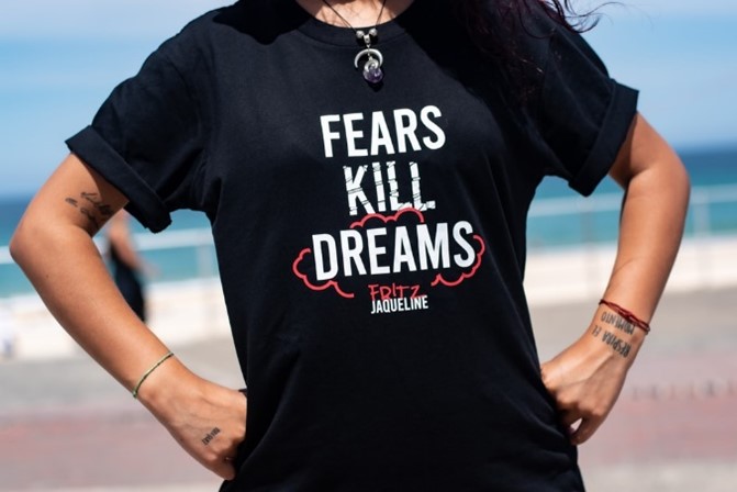 A woman wearing a black shirt with white text that states, 'Fears Kill Dreams.