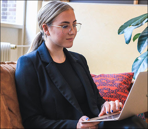 Blonde woman on couch typing on laptop.