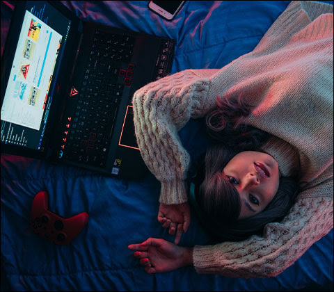 A woman laying on a bed next to an open laptop staring up with arms crossed over her head.